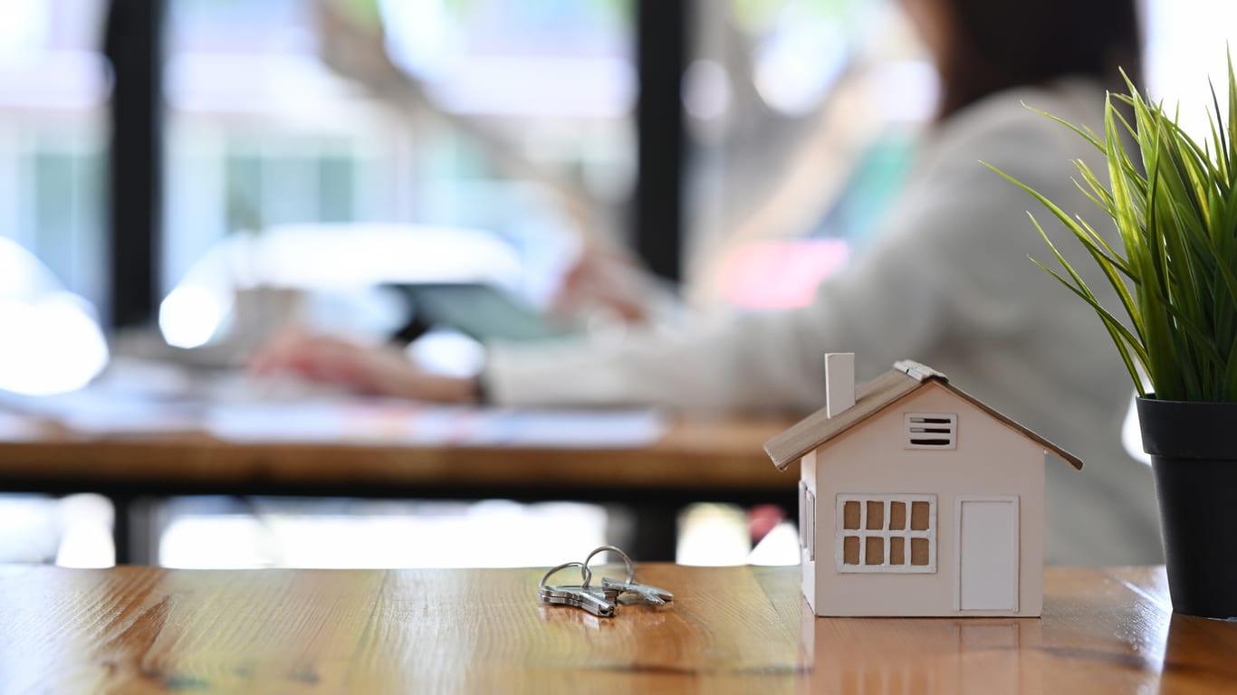 Small house model and house key on wooden table. Concept for a blog discussing closing tips for real estate agents and professionals.