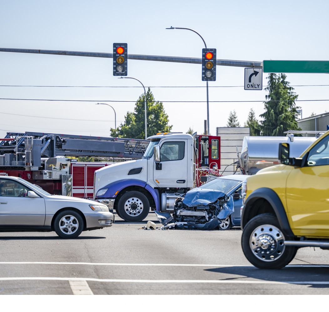 Damaged cars after a car accident crash involving a big rig semi truck with semi trailer at a city street crossroad intersection with traffic light and rescue services to help the injured - Truck Accident Attorney in CT.