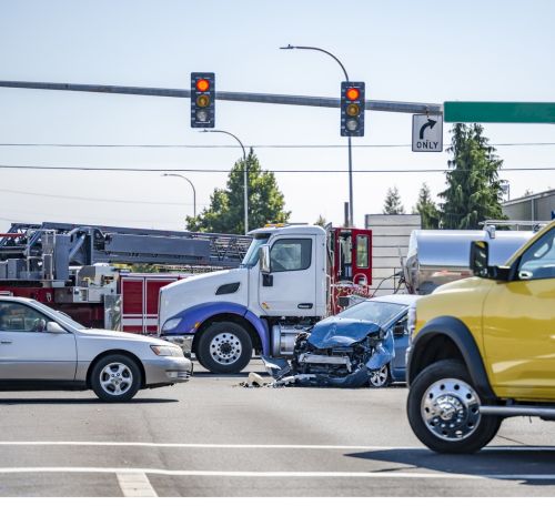 Damaged cars after a car accident crash involving a big rig semi truck with semi trailer at a city street crossroad intersection with traffic light and rescue services to help the injured - Truck Accident Attorney in CT.
